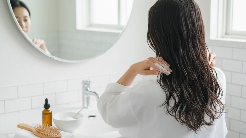 説明:自分の髪を鏡でチェックしながら、サラサラの指通りを実感して微笑む女性